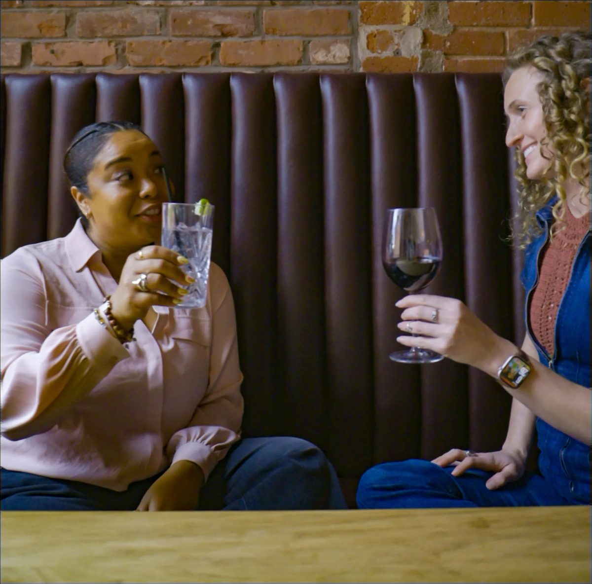Guests sharing drinks in a leather booth against exposed brick.